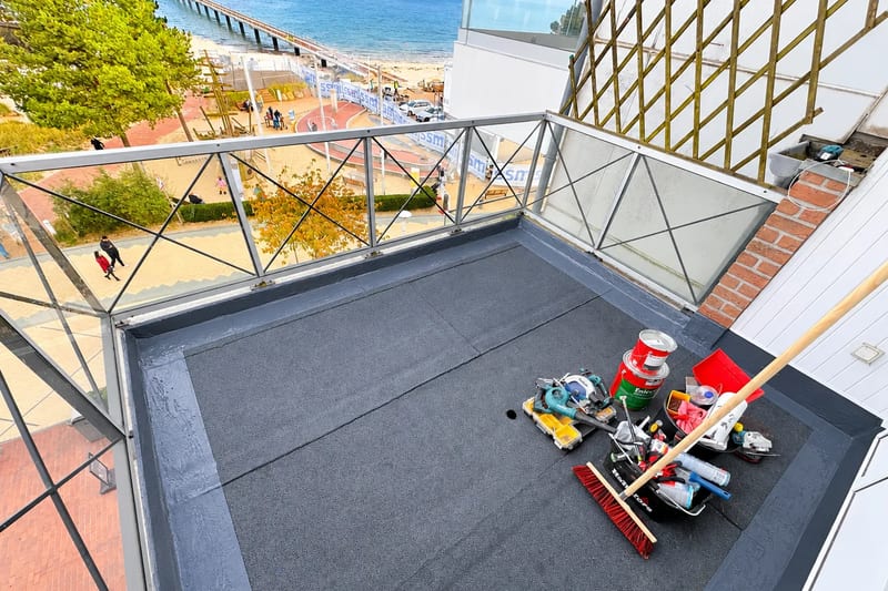 Balkon mit neuer Abdichtung und Glasbrüstung, Werkzeug auf der Fläche, im Hintergrund Strand und Ostsee